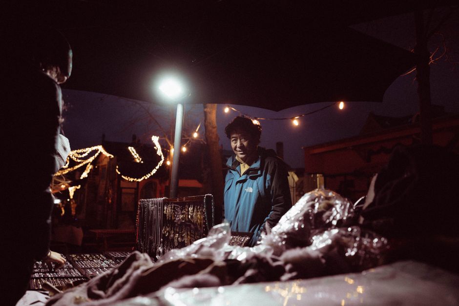 A vendor at a night market interacting with customers under twinkling string lights.