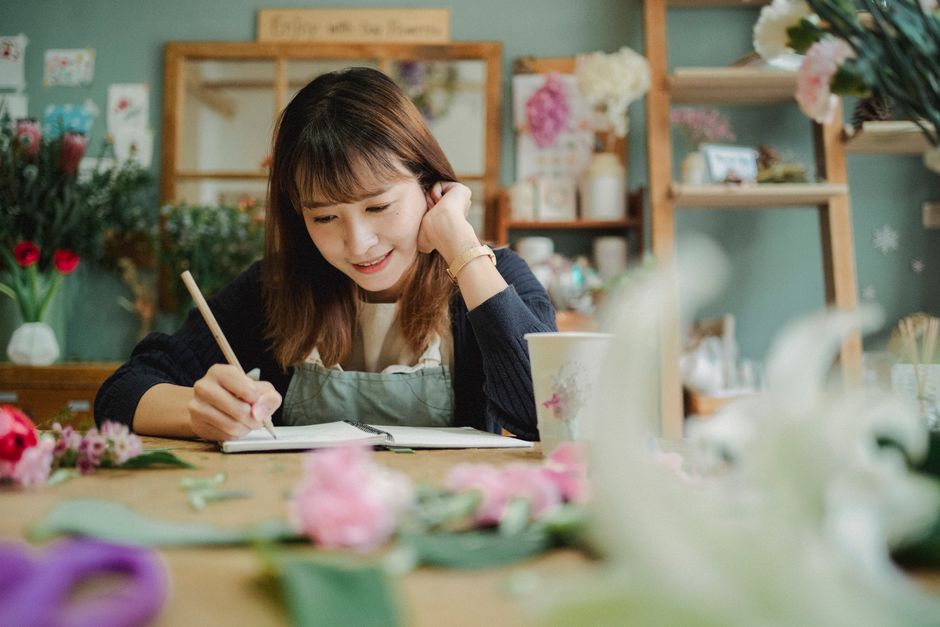 Smiling young female florist in apron writing notes while working in cozy flower shop